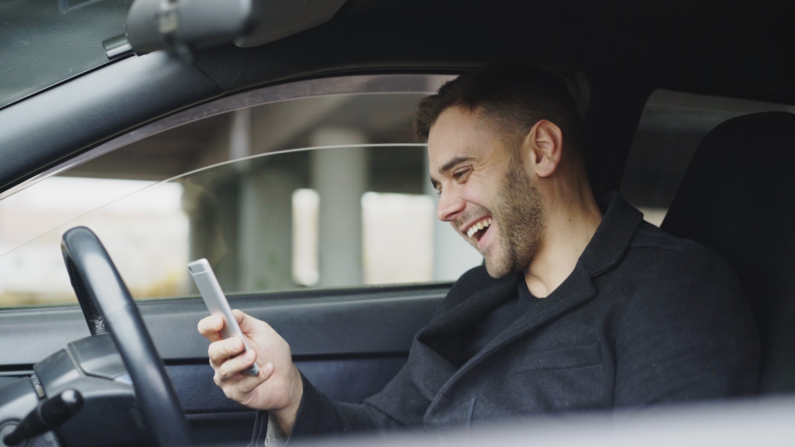 Smiling man looking at his phone in car